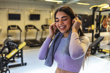 Shot of an attractive young woman standing alone in the gym and listening to music through earphones during her workout.