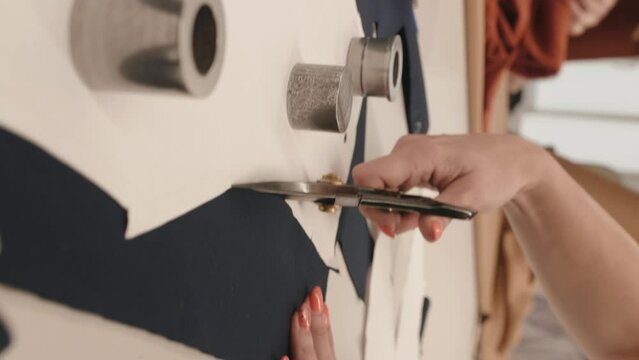 Vertical video of Fashion designer cutting clothes in atelier, working in textile workshop closeup, making fashion dress, using tissue 