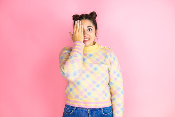 Young beautiful woman wearing casual sweater over isolated pink background covering one eye with...