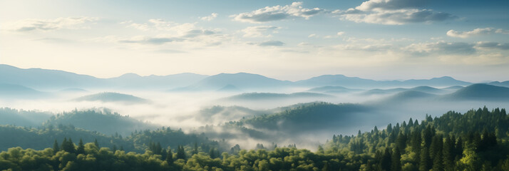 A panoramic view of a mountain range at dawn. Mist weaves through the valleys partially obscures the forested lower slopes. The rising sun illuminates the scene