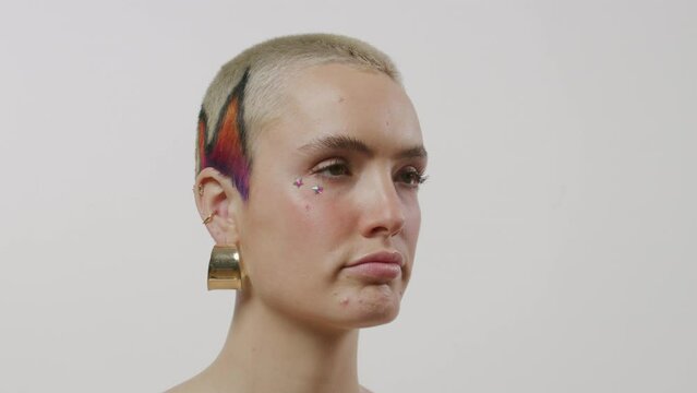 Young person turns to the camera to reveal an eccentric multicolor hairstyle on a white backdrop