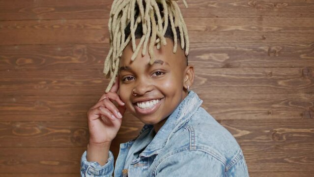 Portrait of a non-binary person smiling at the camera on a wooden backdrop