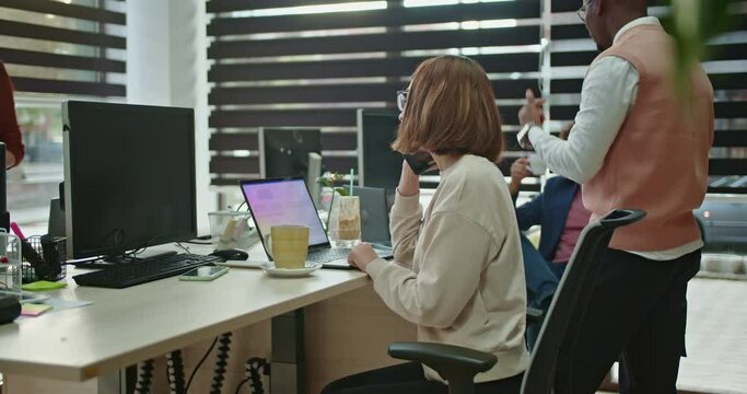 Young, female, business employee working on business strategies and market analysis in a corporate office while having phone call. Multitasking concept.