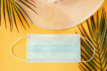 Straw hat and face medical mask on yellow background. Top view. Travel during the coronavirus...