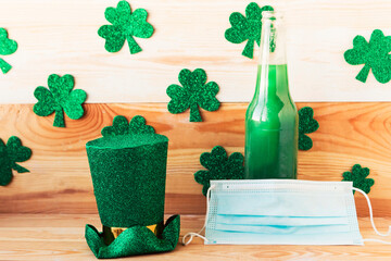 Green beer bottle, leprechaun and face medical mask on wooden background. Corona Patricks Day...