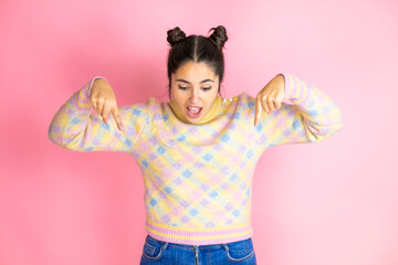 Young beautiful woman wearing casual sweater over isolated pink background surprised, looking down and pointing down with fingers and raised arms