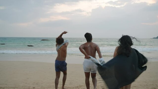Diverse friends run on beach at sunset, happy lgbtq group frolic in ocean spray. Joyful run, splash, play in sea water body positivity in golden hour.