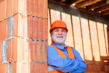 Smiling construction worker in safety vest and helmet at work. Bearded architect builder in protective hard hat. Building and home renovation. Professional foreman, craftsman on construction site.