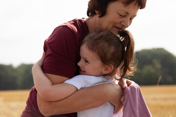 Grandmother and granddaughter hugging in wheat field. Happy family concept.