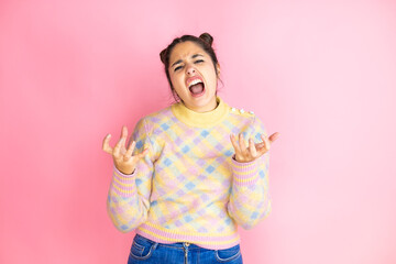Young beautiful woman wearing casual sweater over isolated yellow background crazy and mad shouting and yelling with aggressive expression and arms raised. Frustration concept.