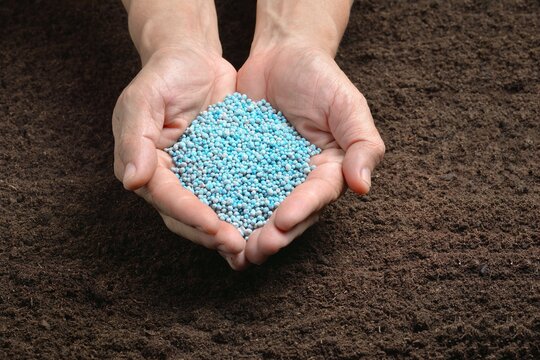 Chemical fertilizers in hand on soil background