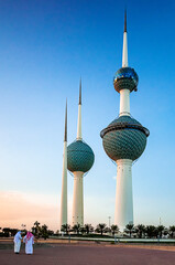 The Kuwait Towers in Kuwait City and two sheikhs from behind discussing and walking at sunset
