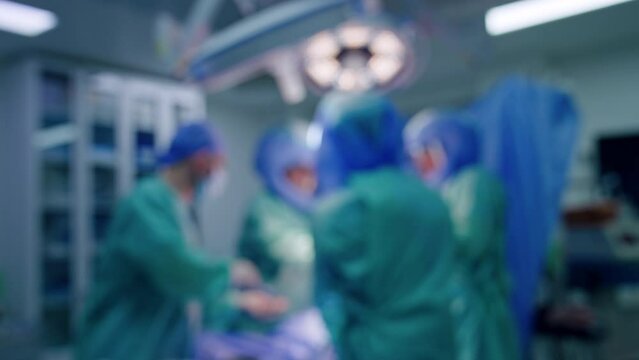 Blurred image of surgical team working in surgery room. Doctors in helmets and assisting medic perform operation on trauma.