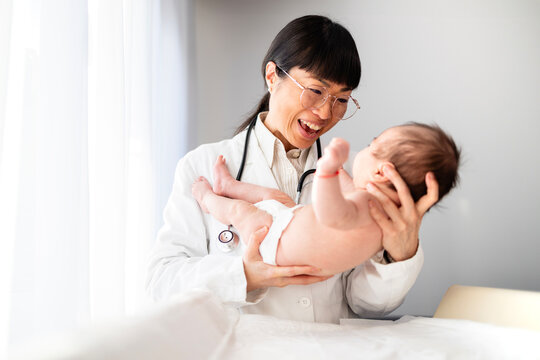 Happy moment of smiling pediatrician doctor holding baby for medical examination and health care.