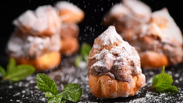 Profiteroles or cream puff with filling,  falling powder sugar topping. Berries, mint on black background. Fresh homemade Cream Puffs, cake, tasty French choux puff, ecler, dessert closeup. Pastries. 