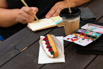 Creative outdoor setting with artist sketching, iced coffee, and pastry topped with fresh berries...