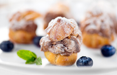 Profiterole or cream puff with filling,  powdered sugar topping with berries, on white background. Fresh homemade Cream Puffs, cake, tasty French choux puff, ecler, dessert closeup. Pastries on plate