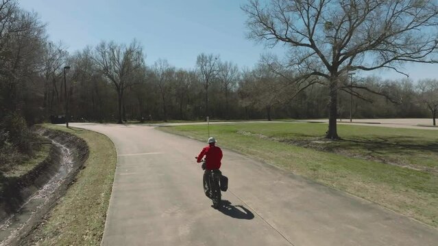 An aerial shot follows a senior male cyclist as he rides an ebike through the Kipper Mease Sports Complex on a clear sunny day in Pasadena, Texas.