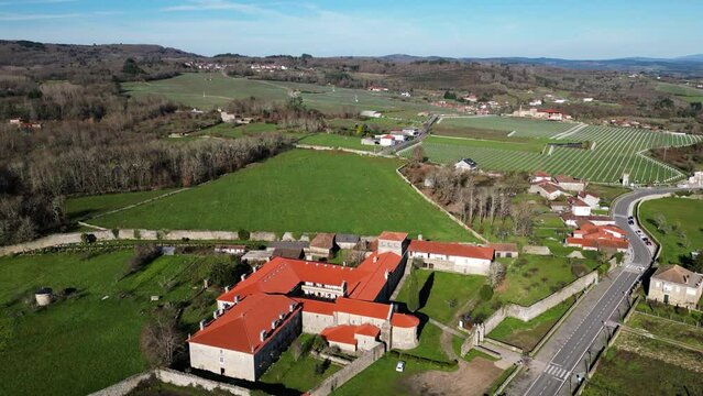Drone orbits around monastery nestled between large open farmland fields in Ourense Spain