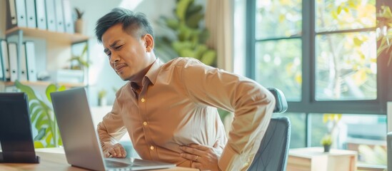 Asian businessman having sick back pain after extra time working with laptop in office. AI generated - obrazy, fototapety, plakaty