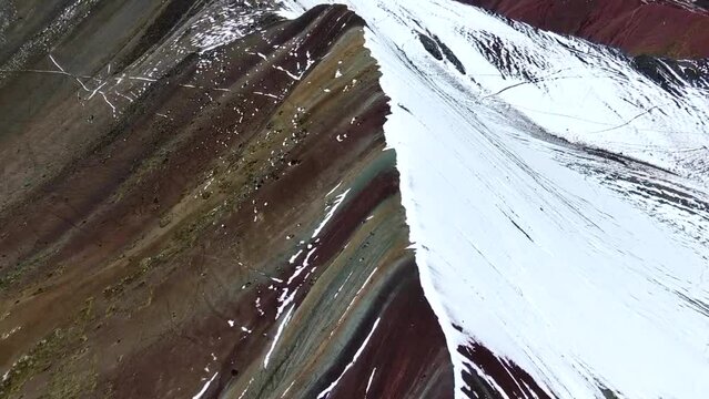 Drone view in Peru flying over rainbow mountain in Cuzco, showing people staring at the half snowed half colored range