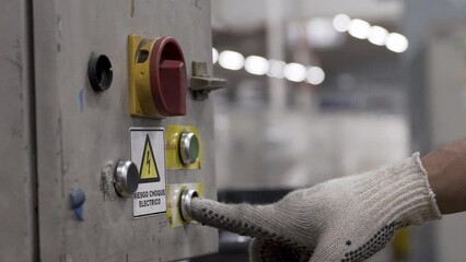 Worker operates industrial button with safety glove in a factory, close-up