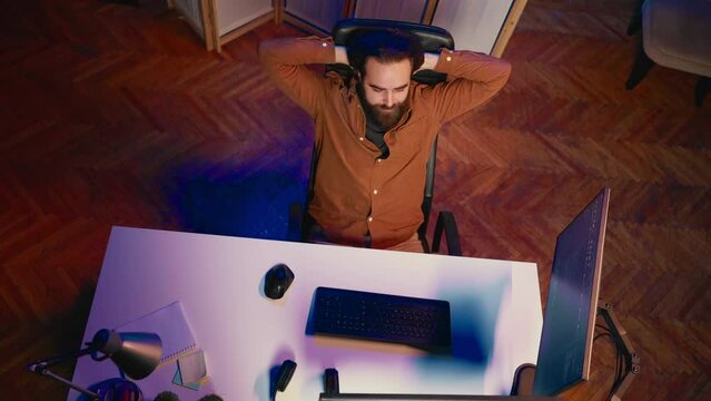 Top down view of IT admin in home office stretching after sitting on desk chair all day. Software engineer loosening up, relaxing after typing on computer for long period of time, aerial shot