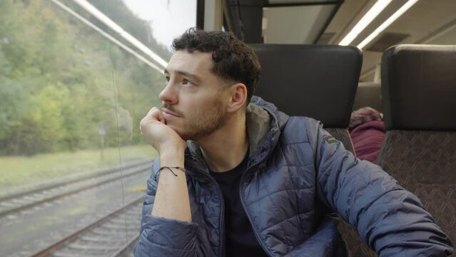 Young caucasian male passenger in train looking out of window in Germany.