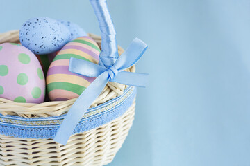 Colorful Easter eggs in a wicker basket on a blue background with a cope space. High quality photo