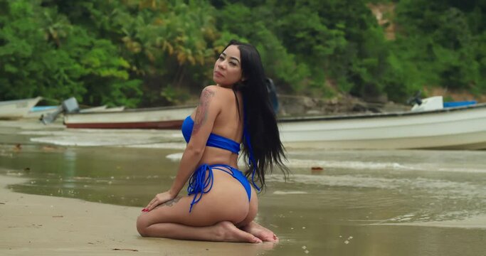 Her blue thong bikini adding a touch of sophistication to the scene along the pristine shores of Maracas Beach, a captivating Latina embodies the epitome of Caribbean elegance,