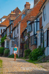 A smiling woman walks along a cobblestone street next to old medieval houses