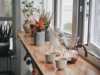 Variety of kitchenware items for coffee on a wooden counter with potted plants