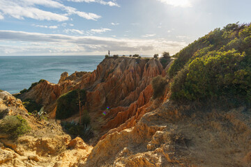 Tourist standing on golden rock cliffs at the coastline of the Atlantic Ocean with near the Cave of Benagil, Algarve, Portugal