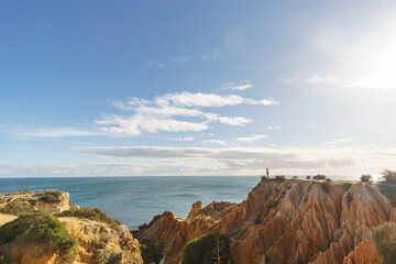 Tourist standing on golden rock cliffs at the coastline of the Atlantic Ocean with near the Cave of Benagil, Algarve, Portugal