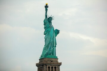 Side view of the iconic Statue of Liberty standing against a cloudy sky