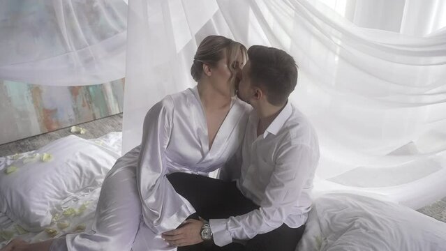 a man and woman are kissing on a bed under a canopy