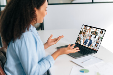 Fototapeta na wymiar Successful brazilian or hispanic businesswoman, company employee, team leader, sitting at workplace in the office in front of a laptop, having online video conference with multiracial team