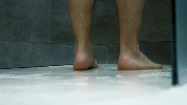 Footage of the white man taking a shower in a modern bath, a ground-level view of feet and water splashes.