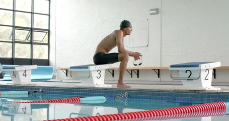 Young biracial male athlete swimmer prepares to dive at an indoor pool