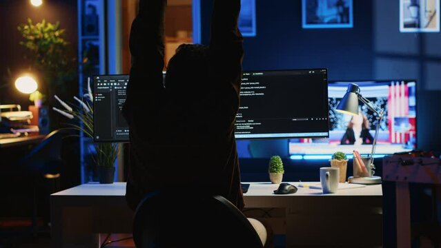 Man doing IT support job from home office, stretching after sitting on desk chair all day. Programmer loosening up, relaxing after typing on computer for long period of time, camera A