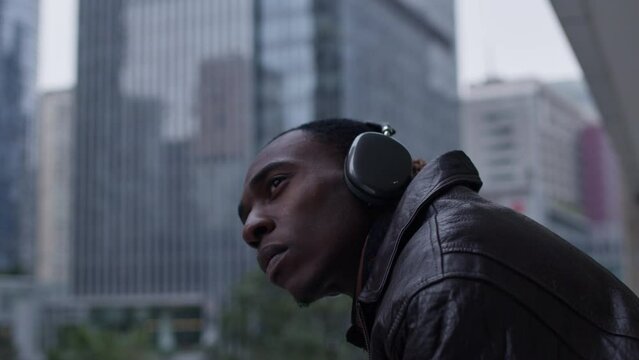 Black Afro-American model seriously looking on urban cityscape of smart city, while listening to music, wearing stylish  headphone.