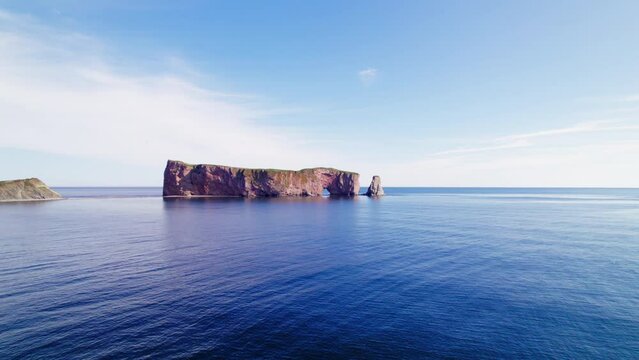 Aerial drone view receding from Perc&eacute; Rock above the Saint Lawrence River during a sunny day