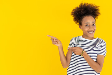 Happy young african woman pointing to copy space over yellow isolated background
