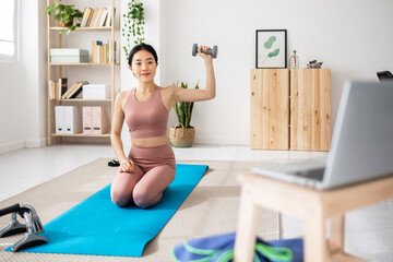 Young asian woman doing workout routine while watching online virtual fitness class. Fitness and healthy lifestyle concept.