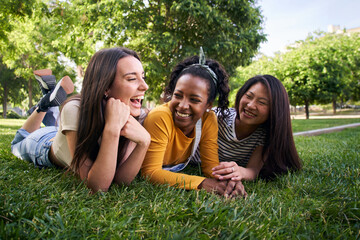 Group multiracial joyful young beautiful women laughing lying chatting having fun on grass in park....