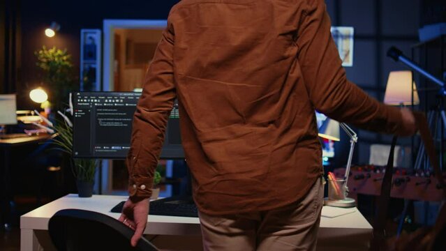Remote software developer arriving in personal office at home, starting job shift with cup of coffee. Teleworker enjoying hot beverage while writing lines of code on computer, camera B