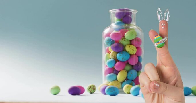 Animation of fingers with easter bunny and easter egg over jar of easter eggs on blue background