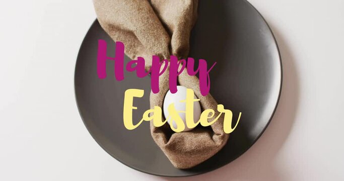 Animation of happy easter text over white easter egg in cloth on black plate on white background