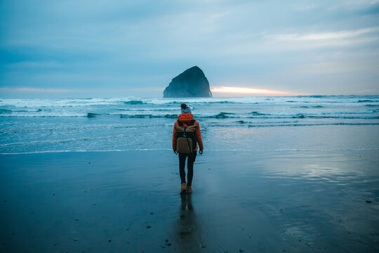Young woman standing in front of Haystack Rock in Cape Kiwanda State Park. Pacific City, Oregon, USA. - Powered by Adobe