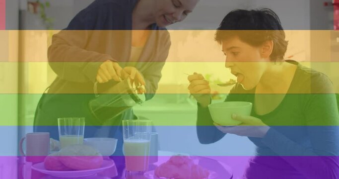 Animation of pride rainbow stripes over happy caucasian lesbian couple having coffee and breakfast